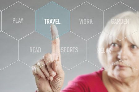Senior woman choosing on virtual digital screen between leisure activities and selects travelの写真素材