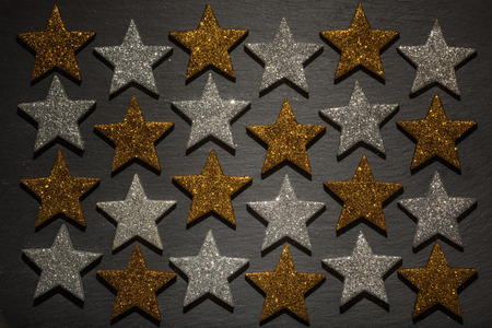 Twenty four silver and golden stars in a row on dark black slate rock background texture.の写真素材