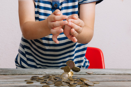 Boy dropping heap of coins on wood table.の写真素材