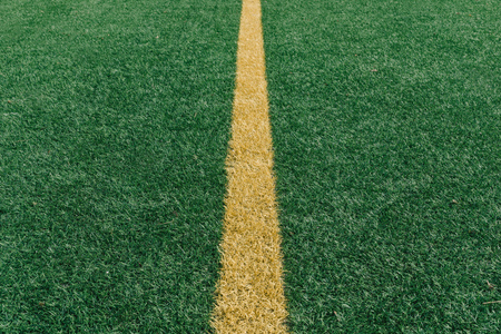 Yellow center line on green artificial grass on turf football field from above, closeup with details and shallow depth of field in opposing sun lightの写真素材