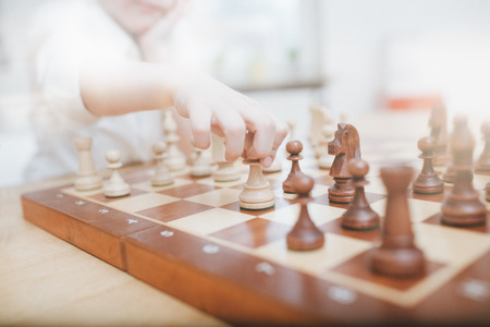 Young boy moving a chess figure on a board, wide angle view with lens flare processing