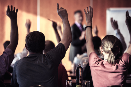 Raised hands and arms of large group of people in class room, audience voting in professional...