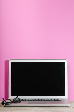 Modern laptop computer in front of pink colored background wall on wooden deskの写真素材
