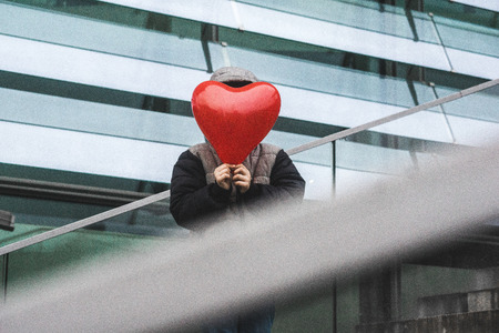 Young boy holding heart shaped red balloon with urban architecture background