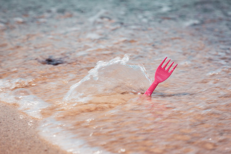 Plastic cutlery fork in sea water on ocean beach, environmental littering concept imageの写真素材