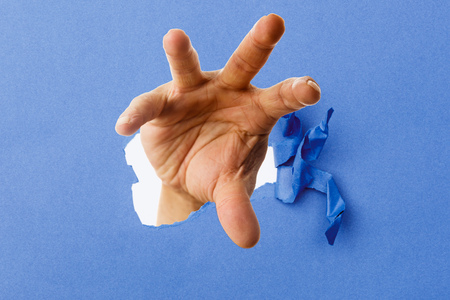 Male hand coming out of ripped piece of paperの写真素材