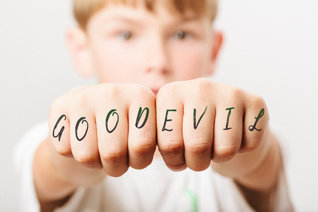 Good and Evil written on fists of Caucasian European school boy with blond hair and brown eyes,...