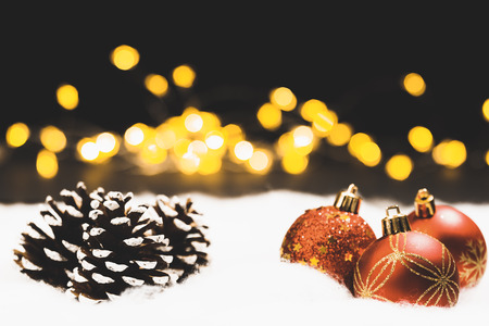 Christmas bauble still life in snow with silent black night background and bokeh lights and pine cones, focus on frontの写真素材