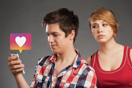 Teenager couple, girl friend spying on boy pressing love button on smart phone in social media app
