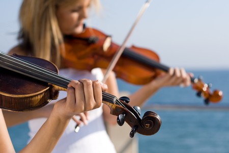 two beautiful young women play violin on beachの写真素材