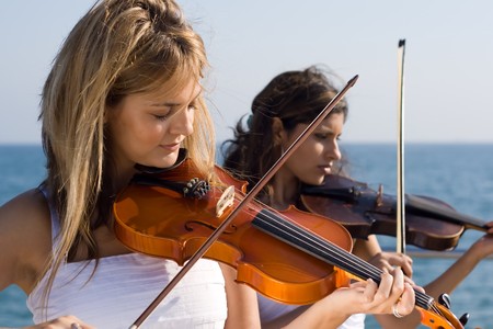 two beautiful young women play violin on beachの写真素材