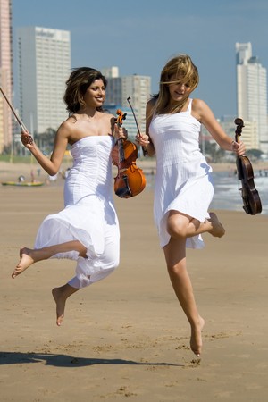two young women jump on beach with violinsの写真素材