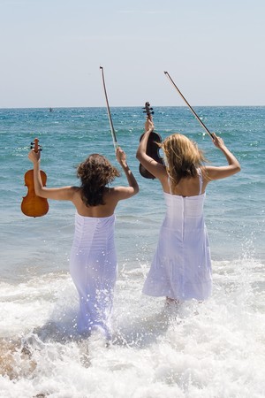 two woman with violin on beach having funの写真素材