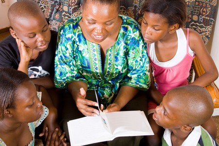 a happy african mother reading a book to her 4 children in living roomの写真素材