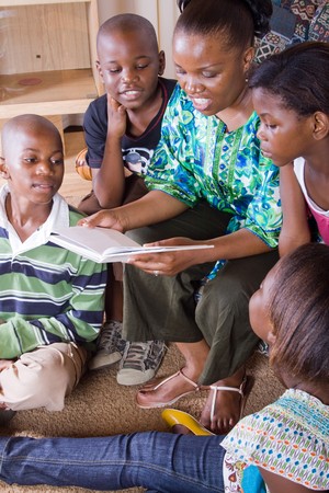 happy african mother reading a book to her 4 children in living roomの写真素材