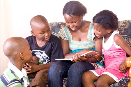 Elder african sister reads to her younger brother and sisterの写真素材