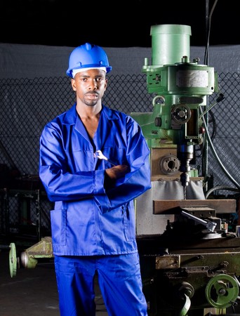African machinist standing next to a drilling machine