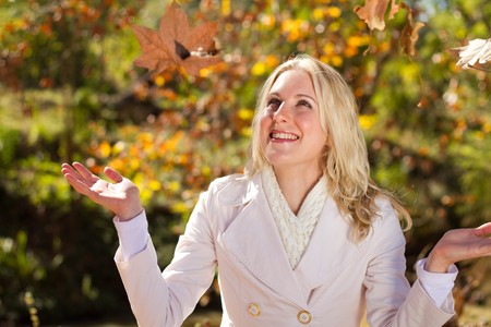 happy woman throwing autumn leaves in forest