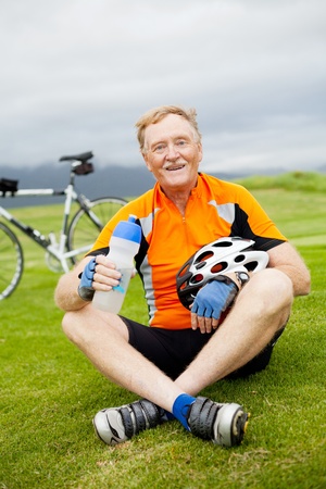 happy active senior bicyclist sitting on grass and restingの写真素材