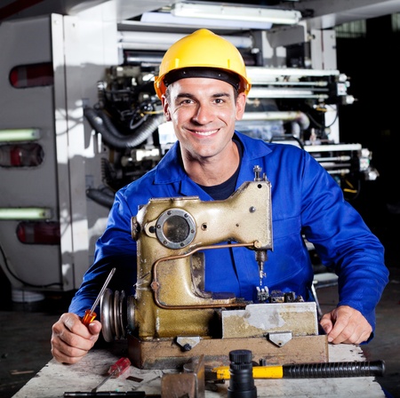 happy mechanic repairing industrial sewing machine in factoryの写真素材
