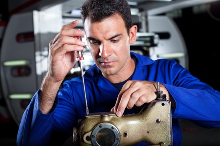 skilled mechanic repairing industrial sewing machine in factory