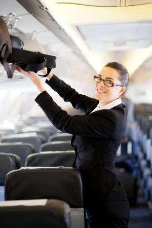 pretty businesswoman putting her luggage into overhead locker on airplane の写真素材