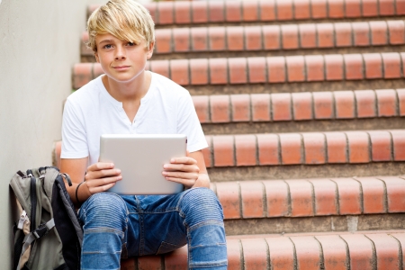 teen boy sitting on stairs and using tablet computer in schoolの写真素材