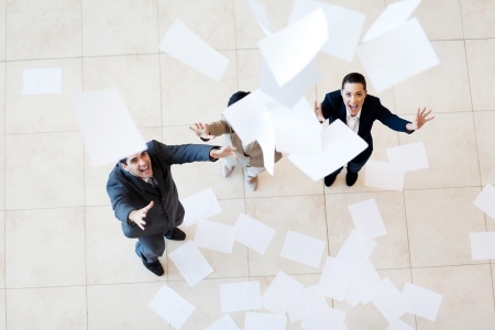 group of businessman and businesswoman catching papers falling from aboveの写真素材