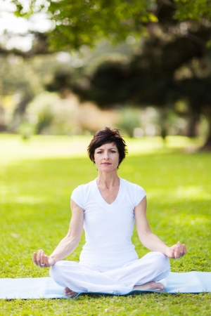 middle aged woman doing yoga meditation outdoorsの写真素材
