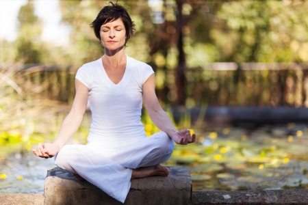 middle aged woman doing yoga meditation outdoorsの写真素材