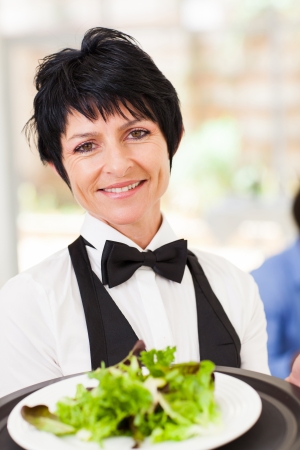 elegant mid age waitress serving salad in restaurantの写真素材