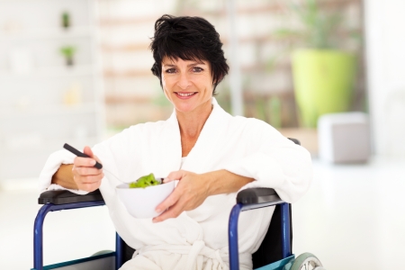 recovering middle aged woman eating salad on wheelchairの写真素材