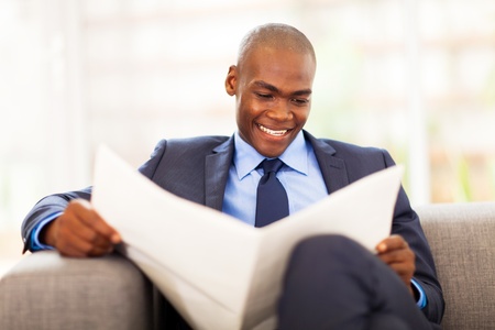 handsome african corporate worker reading newspaper in officeの写真素材
