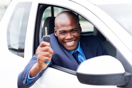 happy african vehicle buyer inside his new car with car key
