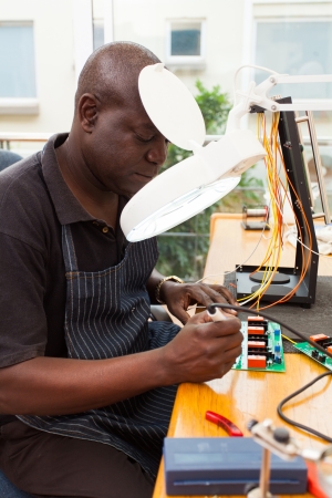 senior african technician repairing a circuit board under electronic magnifying glassの写真素材