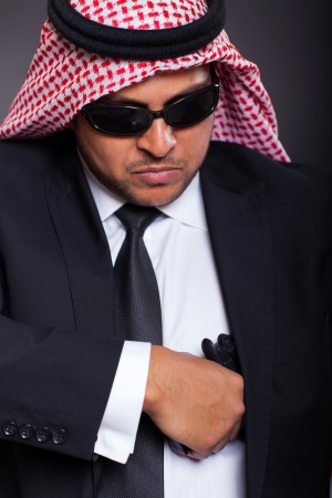 dangerous middle eastern hitman drawing his handgun on black backgroundの写真素材