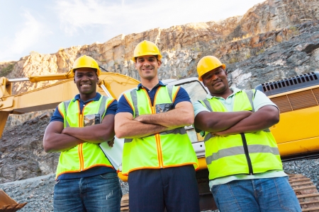 group of quarry workers standing next to excavator with arms crossedの写真素材