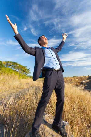 excited young businessman on top of rock with arms outstretched outdoorsの写真素材