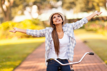 pretty young woman enjoying riding bike at the park with arms outstretched pretty young woman enjoying riding bike at the park with arms outstretched
