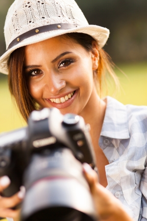 beautiful young woman holding camera outdoors smilingの写真素材