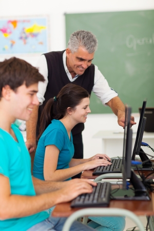 cheerful middle aged teacher helping high school students with computer workの写真素材