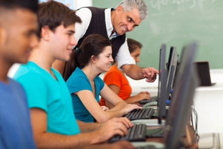 friendly middle aged teacher teaching computer to high school studentsの写真素材