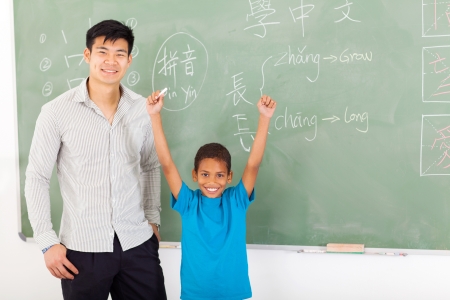 happy african boy with hands up after writing answer on chalkboardの写真素材