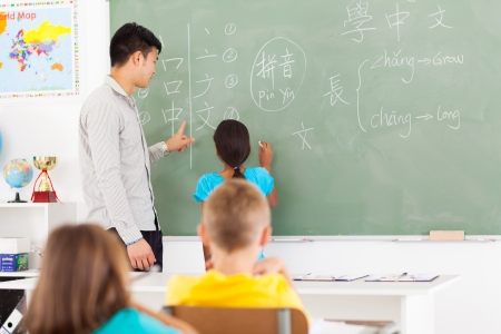 elementary school student writing answer on the board with teacher standing next to herの写真素材