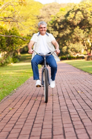 senior man riding bicycle outdoors in parkの写真素材