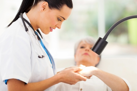 friendly dermatologist examining senior woman's skin under lightの写真素材