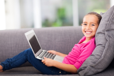 cheerful little girl with a laptop computer lying on couchの写真素材