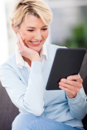 attractive mature woman reading a book on tablet computerの写真素材