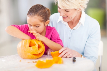 cute granddaughter helping her grandmother making halloween pumpkin at homeの写真素材