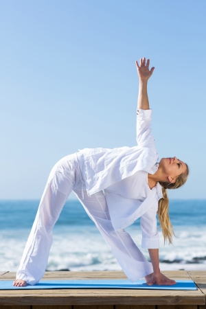pretty middle aged woman doing yoga pose on beachの写真素材
